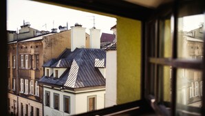 A view through a window of a building with multiple floors, featuring a mix of architectural styles and a variety of roof shapes. - Hotel Eden (Kraków)