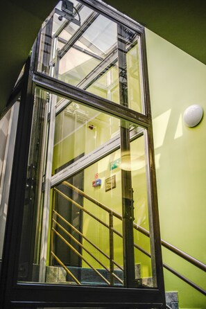 Un ascenseur en verre avec des garde-corps métalliques et un mur végétal.