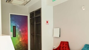 Ein modernes Interieur mit einer Tür im geometrischen Muster, einem samtigen roten Sessel, einem türkisfarbenen Sofa und einer wandmontierten Leuchte.