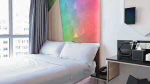 Et hotelværelse med en seng, et skrivebord med telefon og et farverigt geometrisk vægdesign.