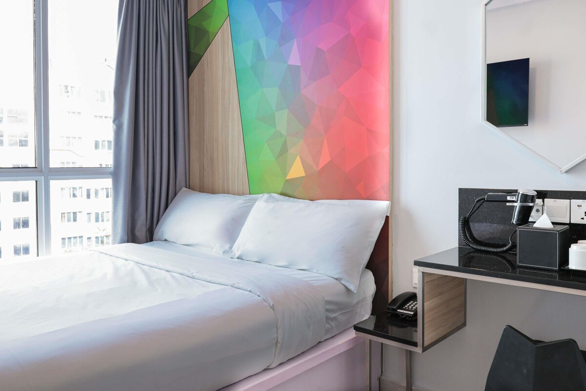 A hotel room with a bed, a desk with a phone, and a colorful geometric wall design.