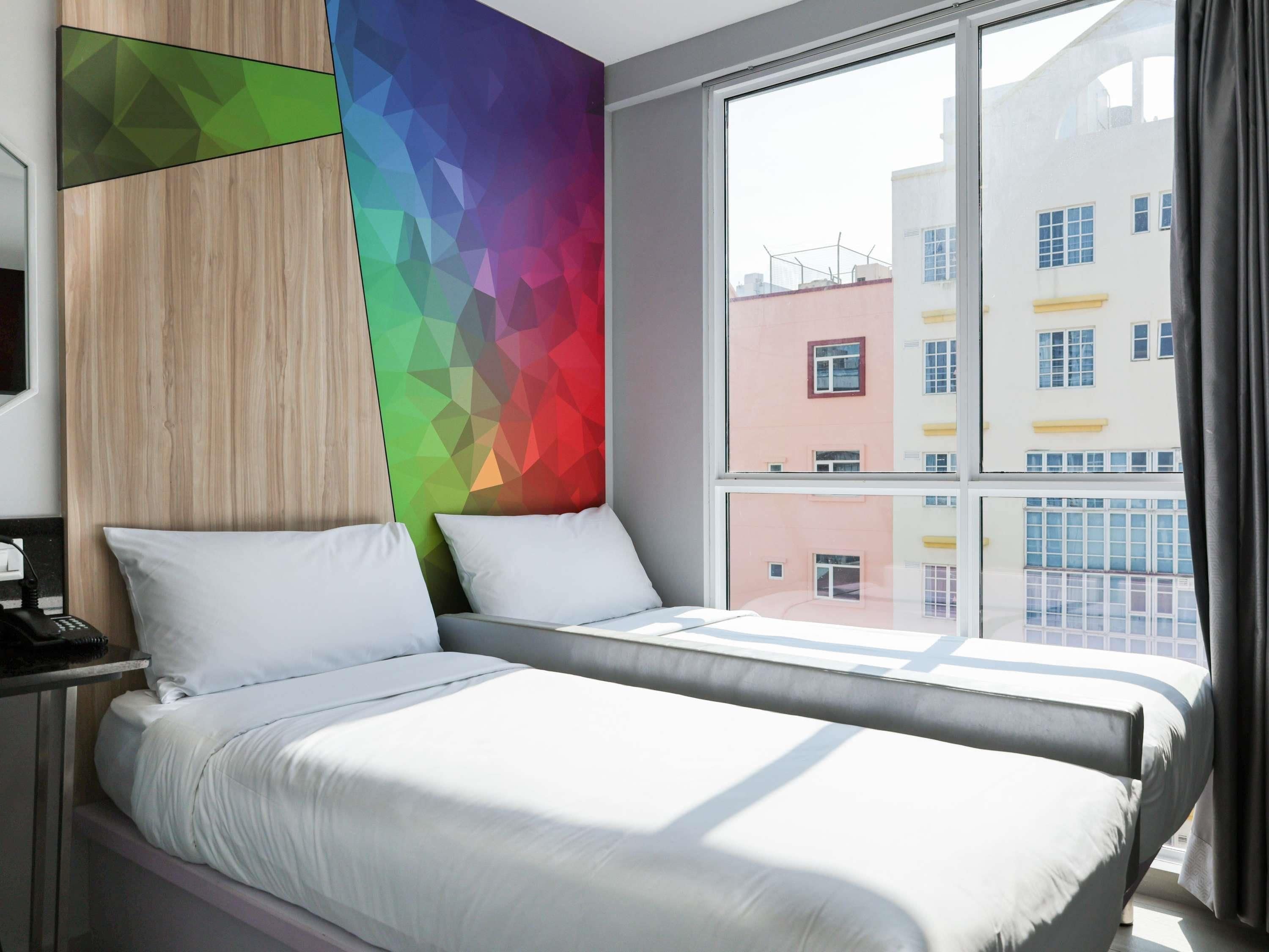 A hotel room with a bed, a bedside table, and a window with a view of buildings.
