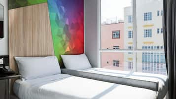 Een hotelkamer met een bed, nachtkastje en een raam met uitzicht op gebouwen.
