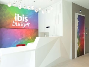 A reception desk with a colorful geometric wall design and a sign that reads 'ibis budget.' - ibis budget Singapore Olive (Singapore)