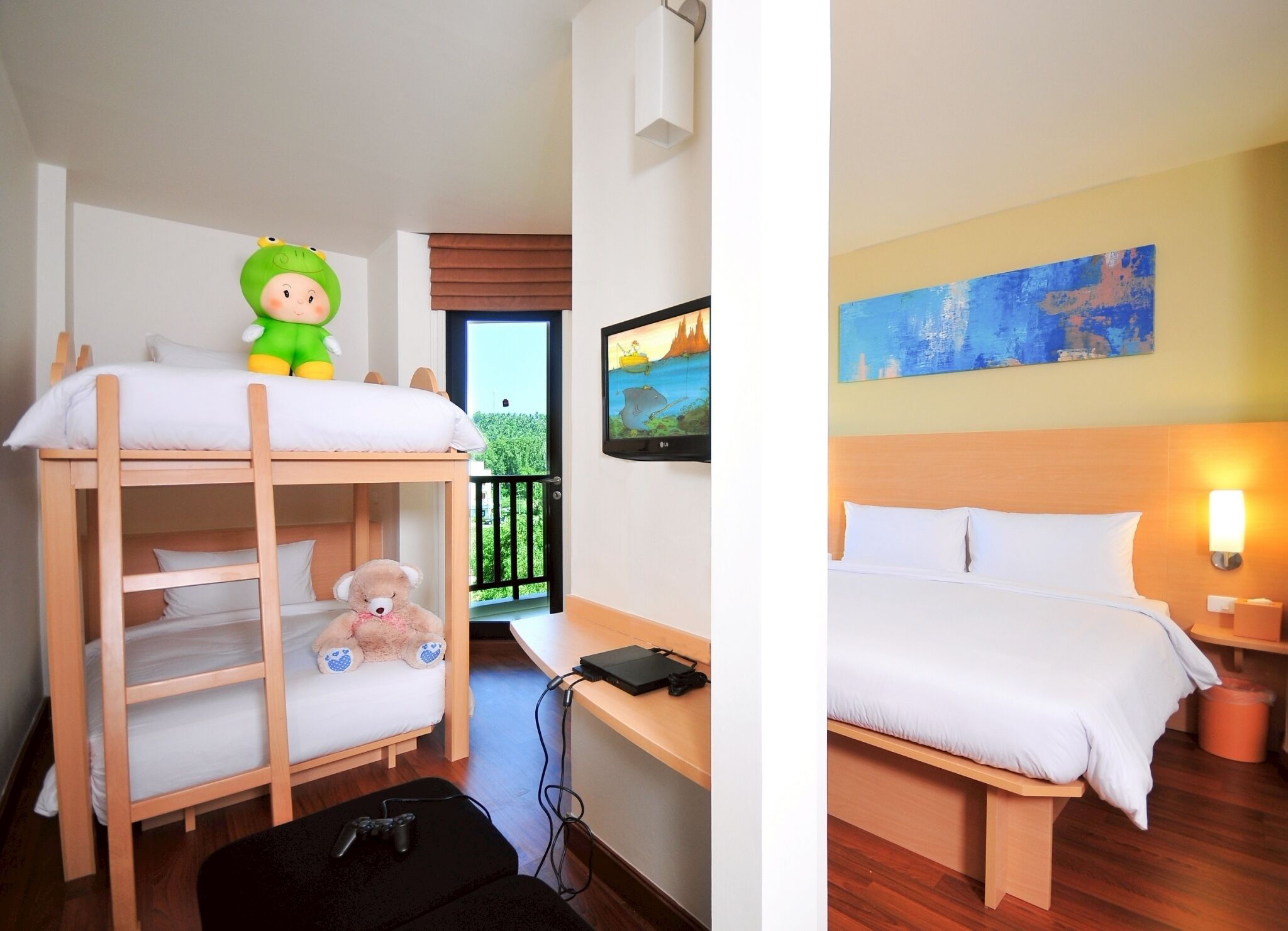 A hotel room with a bunk bed, a desk with a laptop, a teddy bear, and a television.