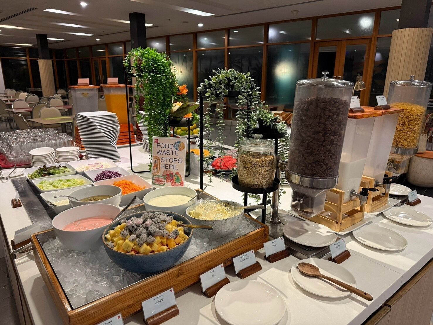 Montaje de bufé con distintas estaciones de comida, que incluyen un bol de frutas, ensalada y un dispensador de bebidas.