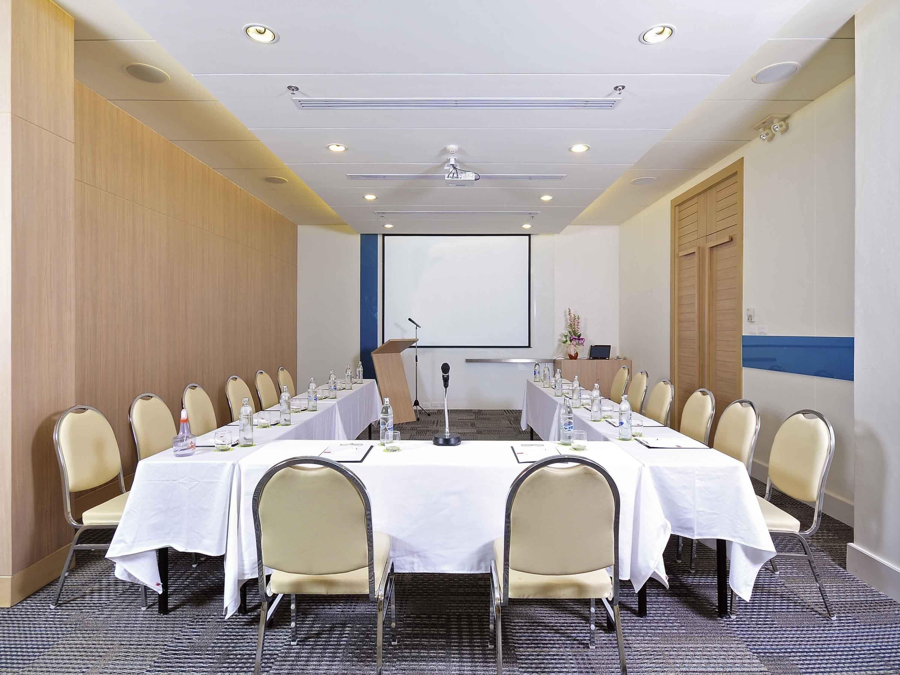 A conference room with a long table, chairs, a podium, a screen, and a carpeted floor.