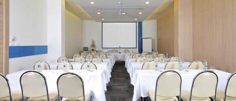 A conference room with multiple tables, chairs, a projector screen, and a carpeted floor.