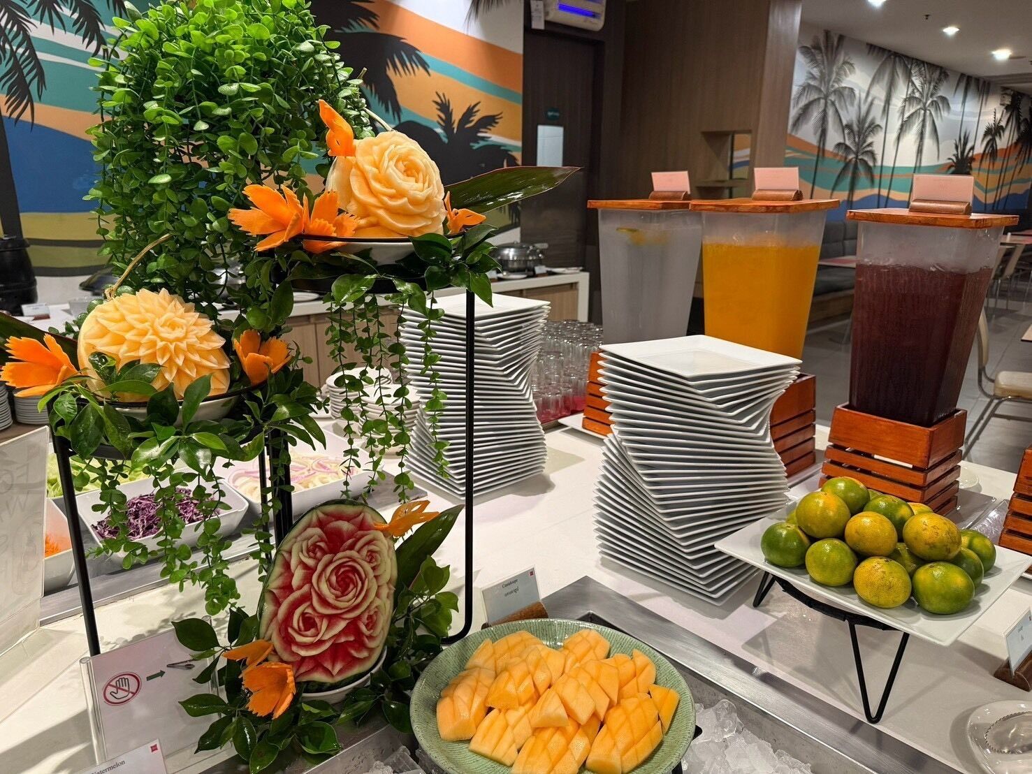A buffet setup with carved fruits, stacked plates, and a fruit display.