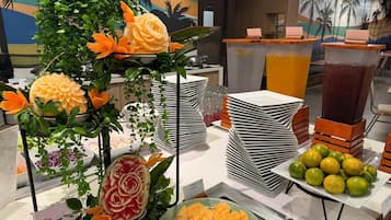 A buffet setup with carved fruits, stacked plates, and a fruit display.