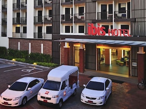 A hotel with a modern facade, multiple balconies, and a parking area with three vehicles. - ibis Phuket Kata (Karon)