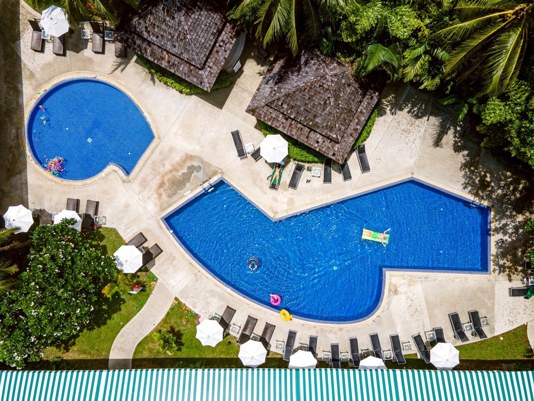 A pool area with two pools, lounge chairs, umbrellas, and a thatched-roof structure.