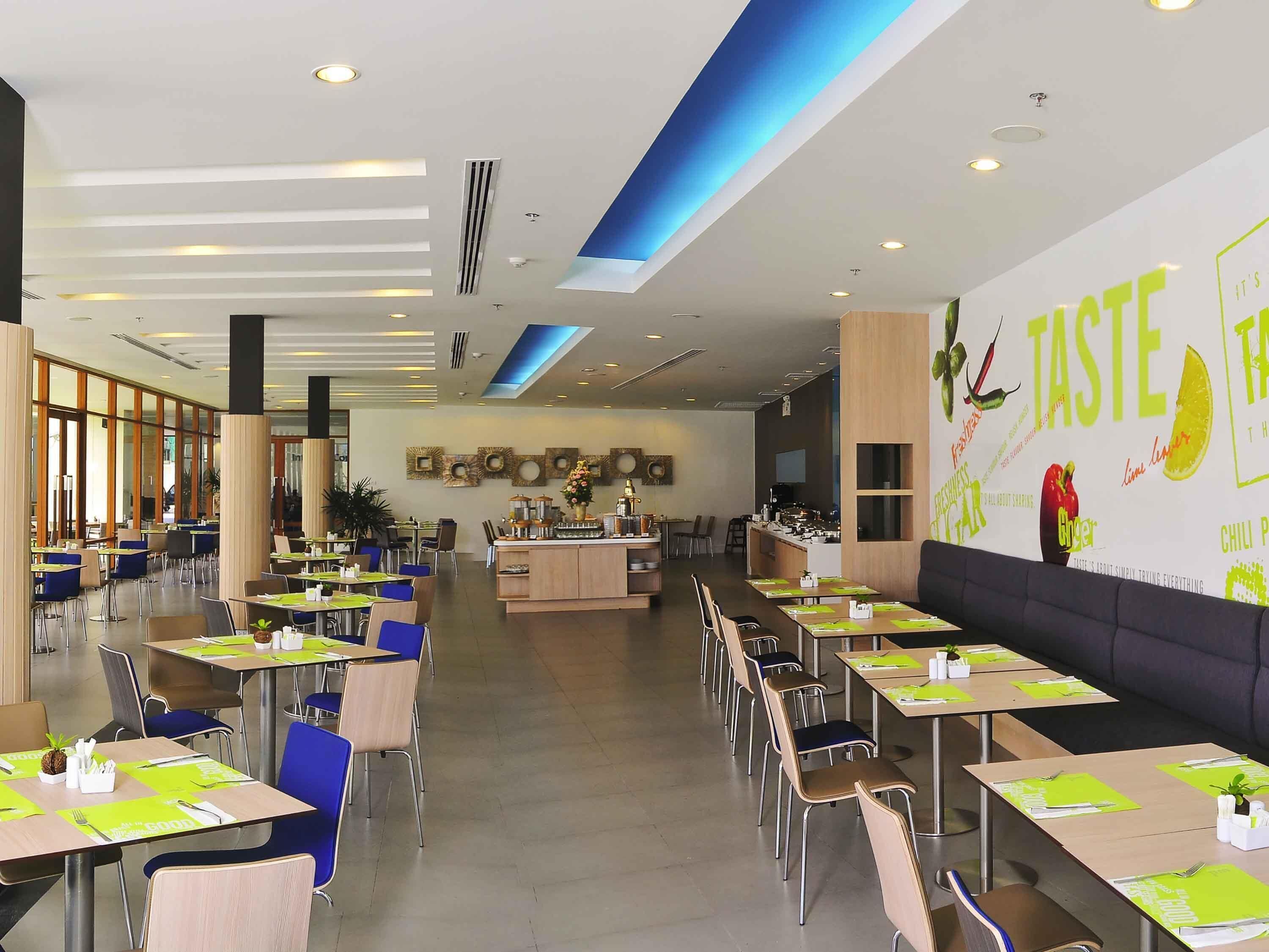 A modern dining area with tables and chairs, a central island with a bar, and a wall with food-related graphics.