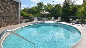 A clear swimming pool with a stone wall, lounge chairs, and a covered table.
