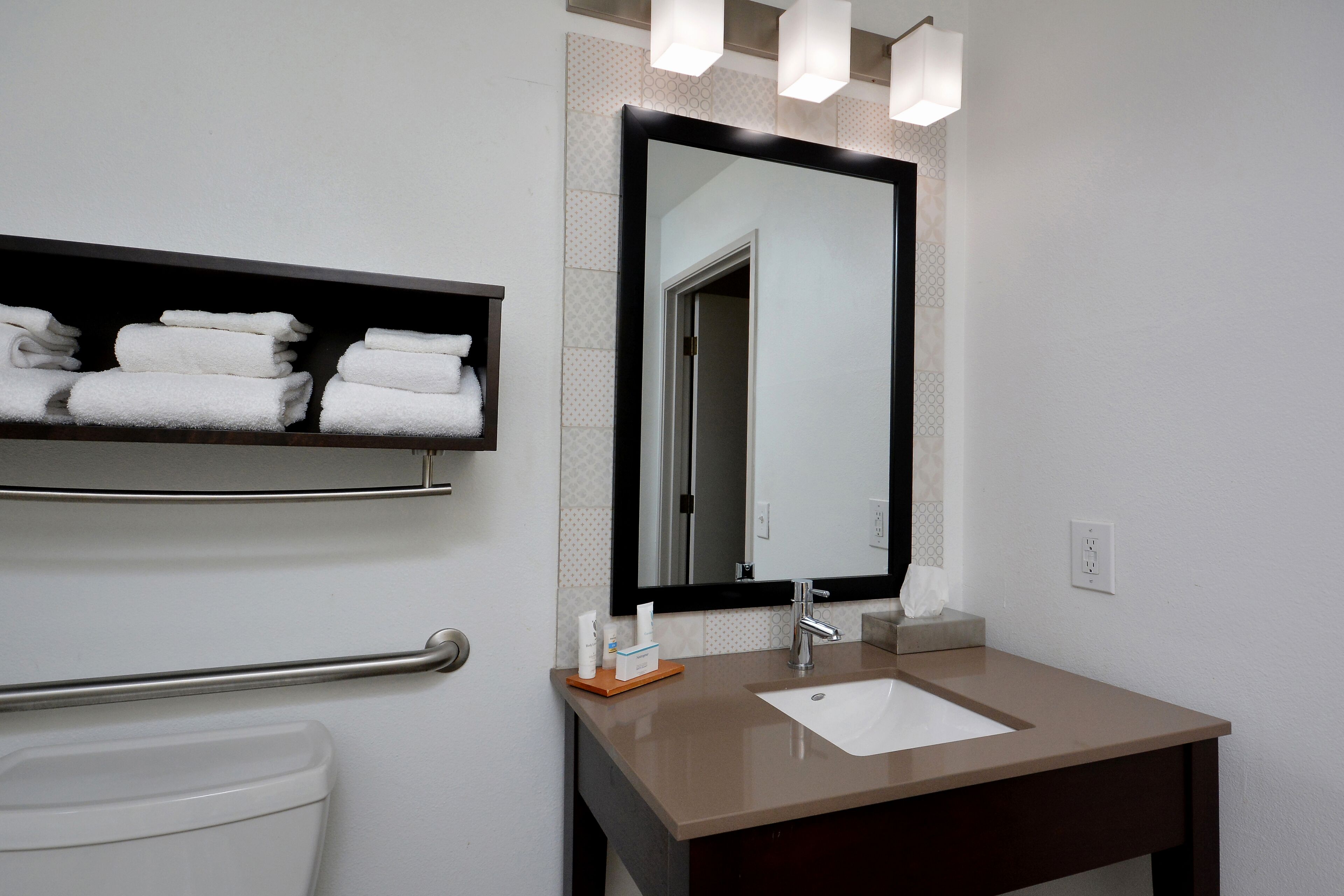 Un baño con un lavabo blanco, un espejo y un perchero con toallas dobladas.
