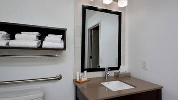 Un baño con un lavabo blanco, un espejo y un perchero con toallas dobladas.