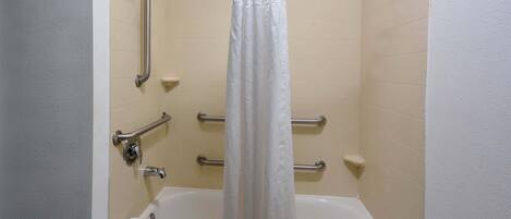 A bathroom with a bathtub, grab bars, and a shower curtain.