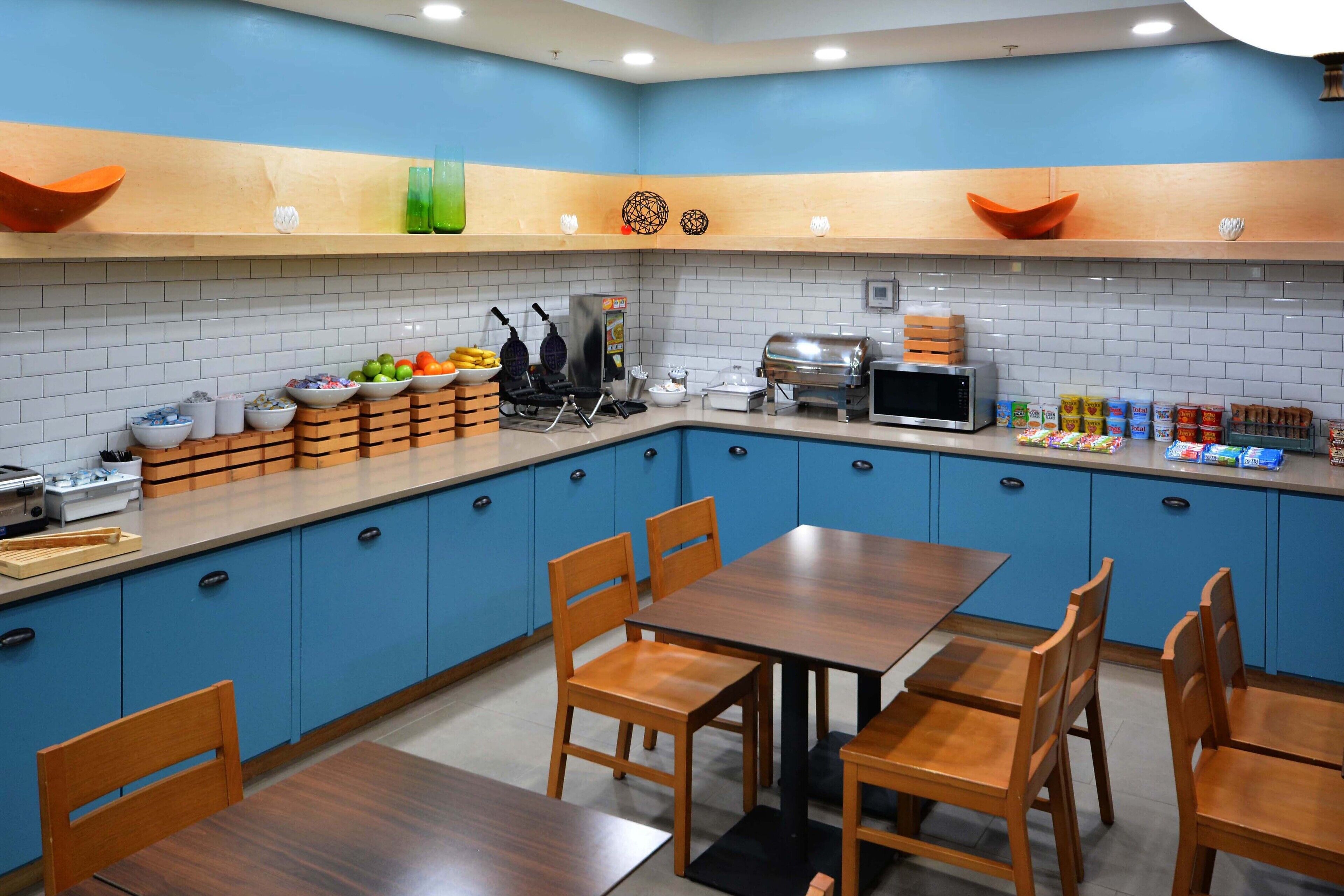 A modern kitchen with blue cabinets, a wooden dining table, and various kitchen appliances.