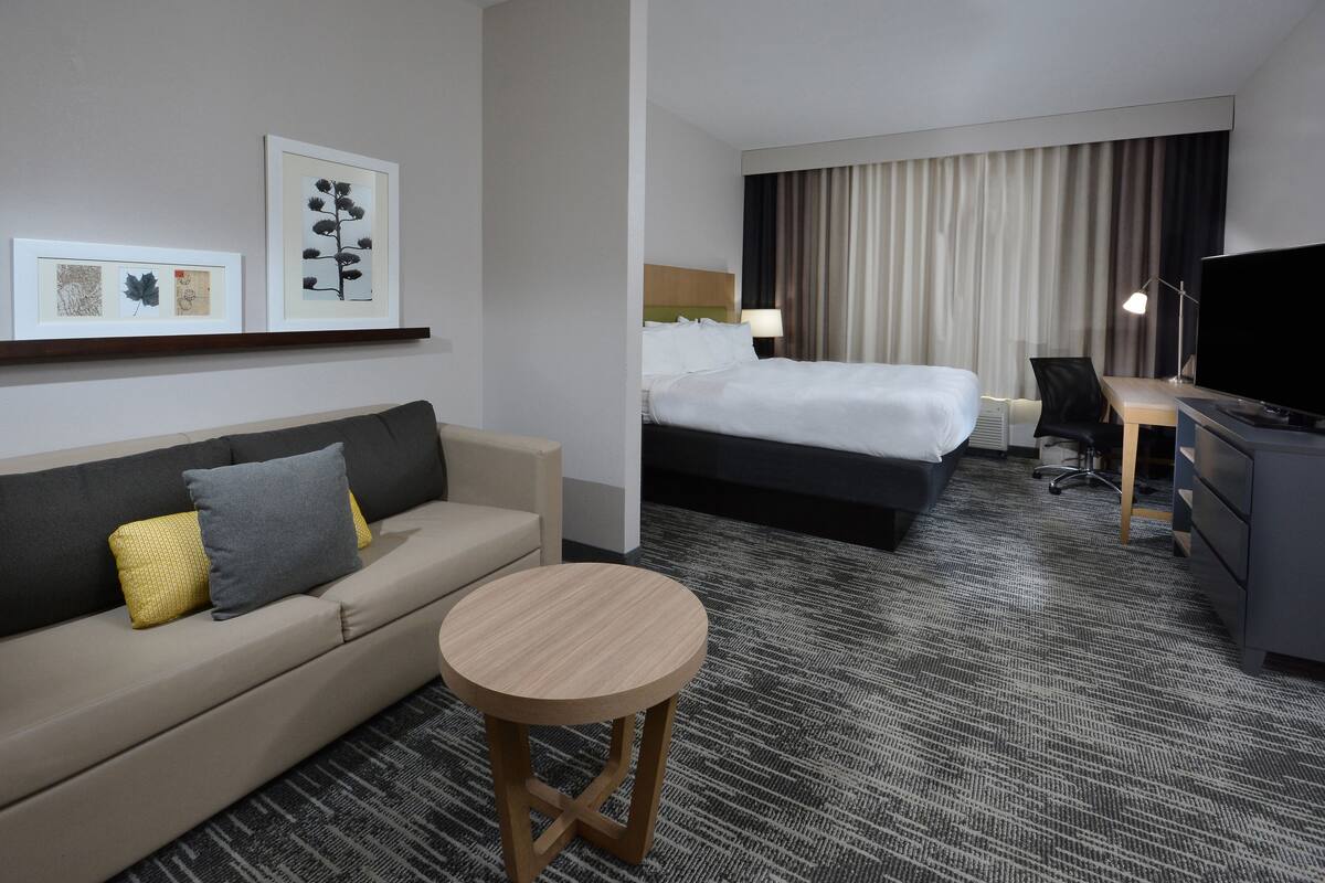 A hotel room with a bed, a sofa, a desk, a TV, and framed artwork on the wall.