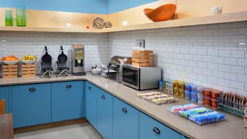 A kitchen with blue cabinets, a microwave, waffle maker, and various food items on the counter.