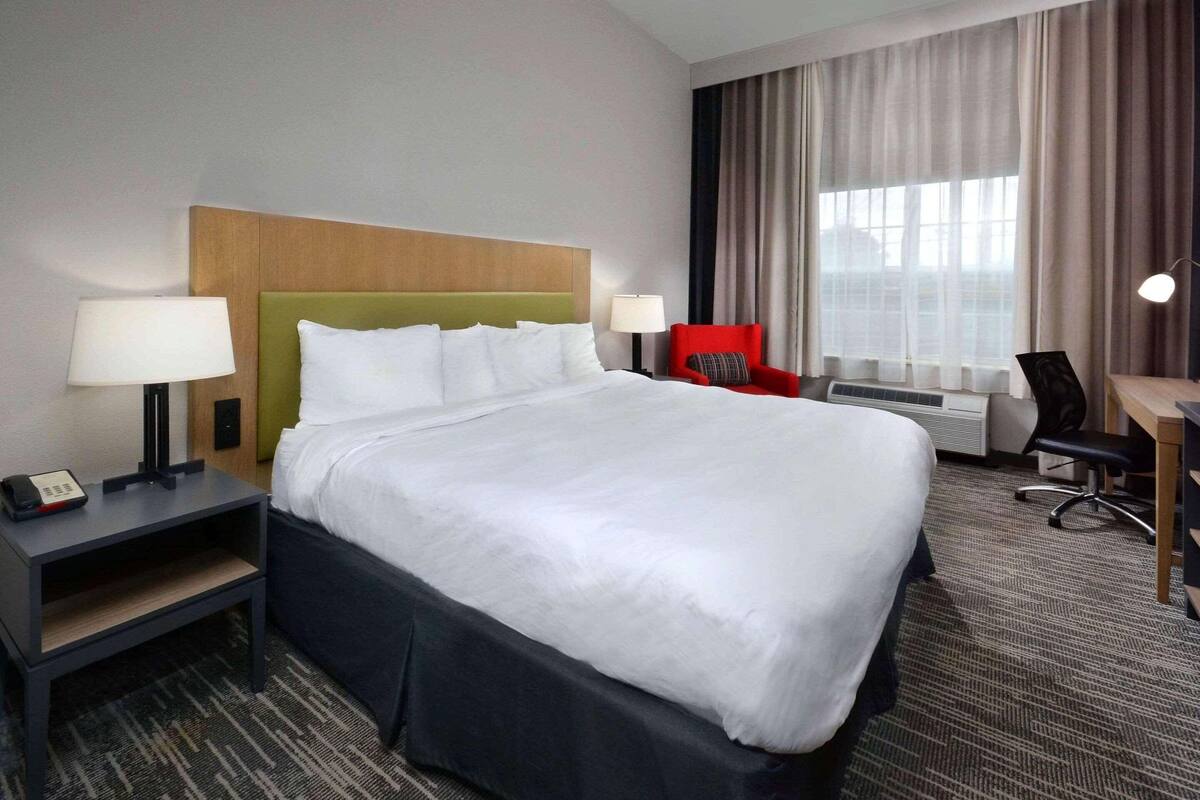 A hotel room with a large bed, a desk, a chair, a lamp, and a window with curtains.