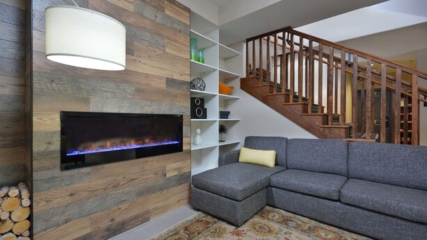 A living room with a fireplace, grey sectional sofa, wooden staircase, and a white shelving unit.