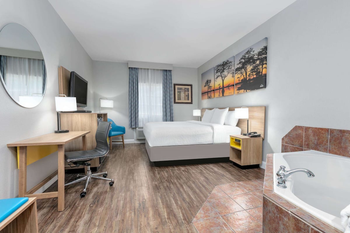 A hotel room with a bed, desk, chair, TV, and a bathroom with a bathtub.