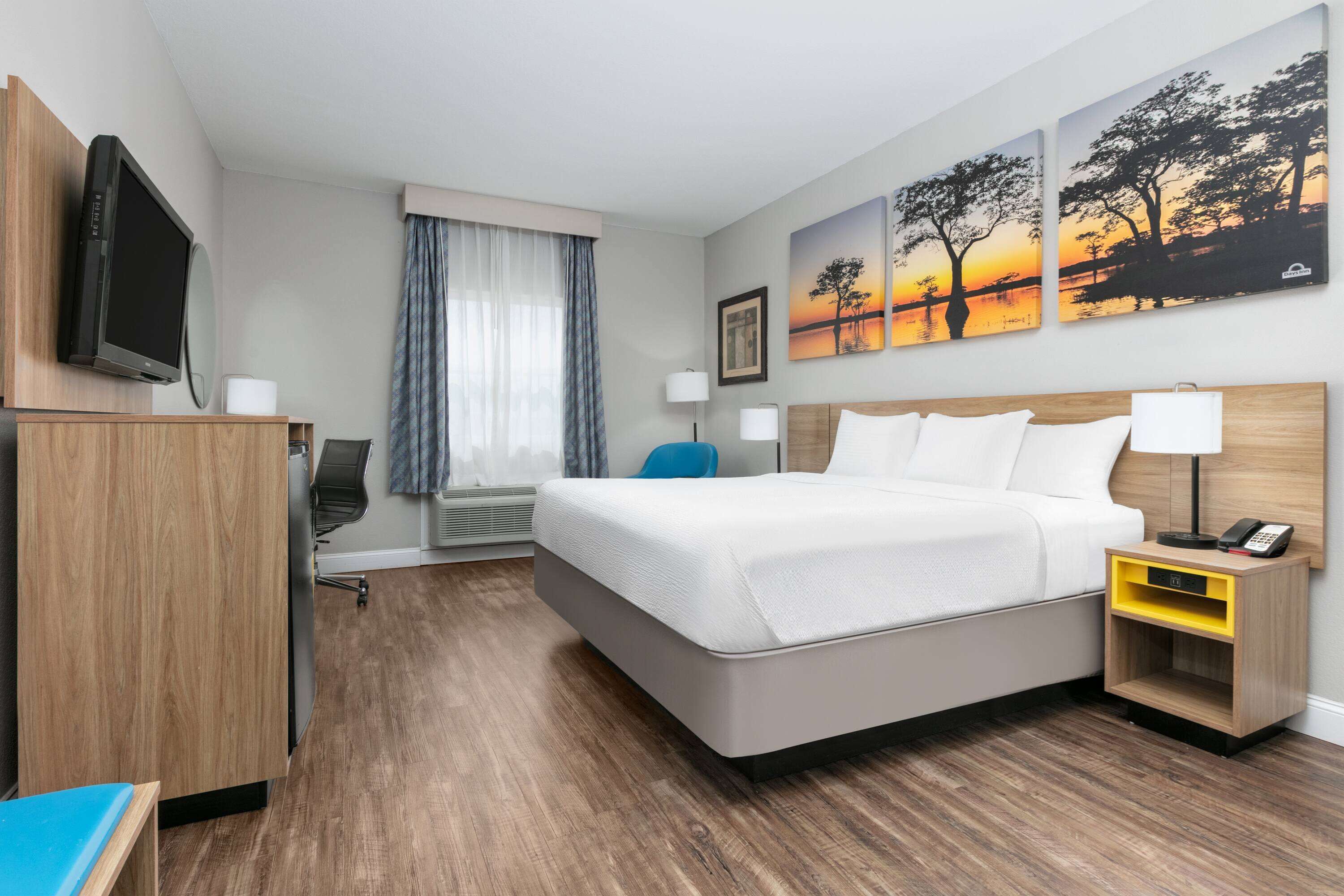 Una habitación de hotel con cama, mesitas de noche, televisión, escritorio y ventana con cortinas.