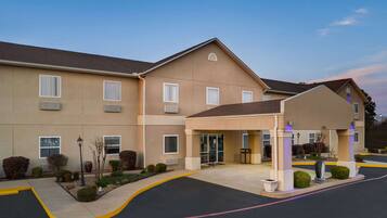 A multi-story hotel with a covered entrance, a landscaped front yard, and a parking area.