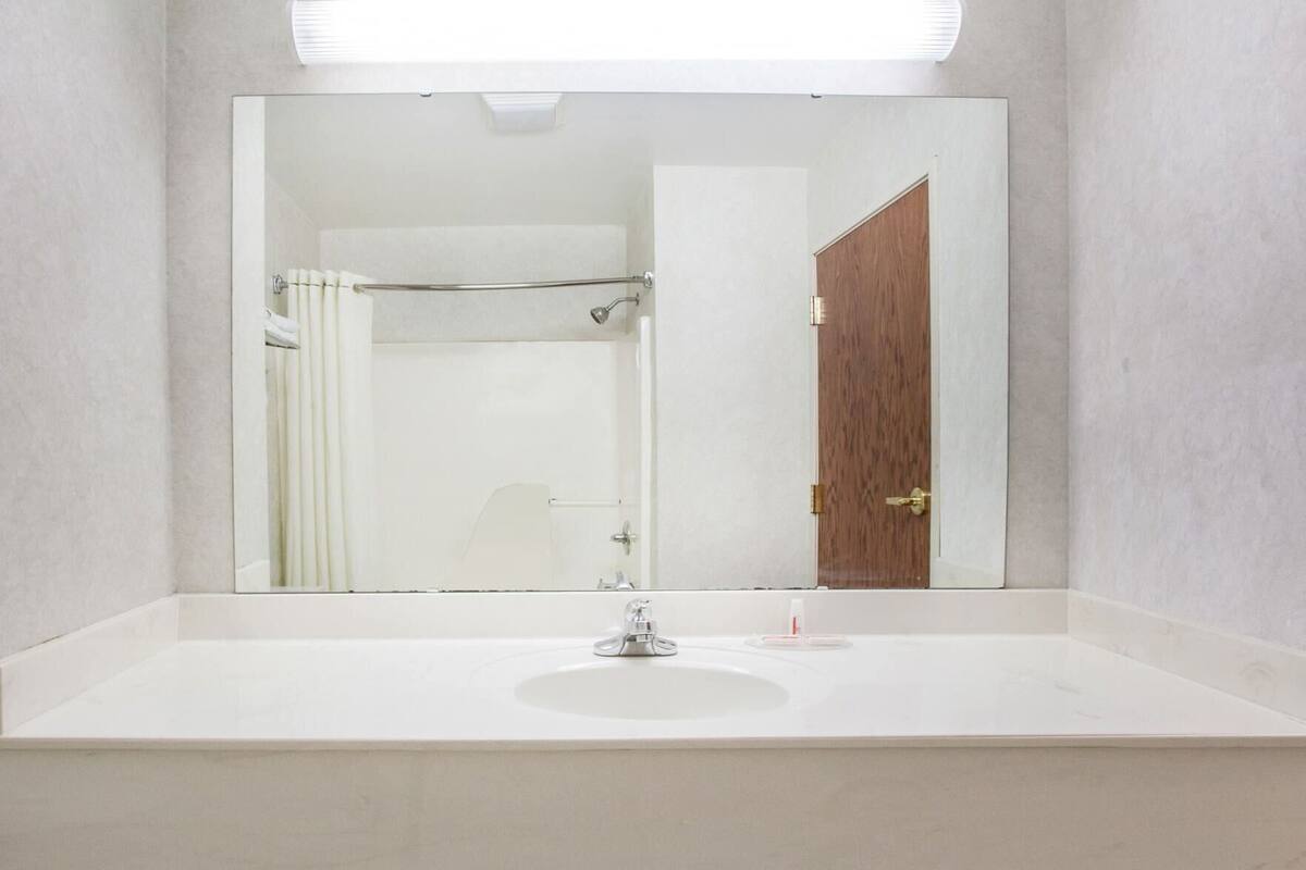 A bathroom with a large mirror, a sink, a shower curtain, and a wooden door.