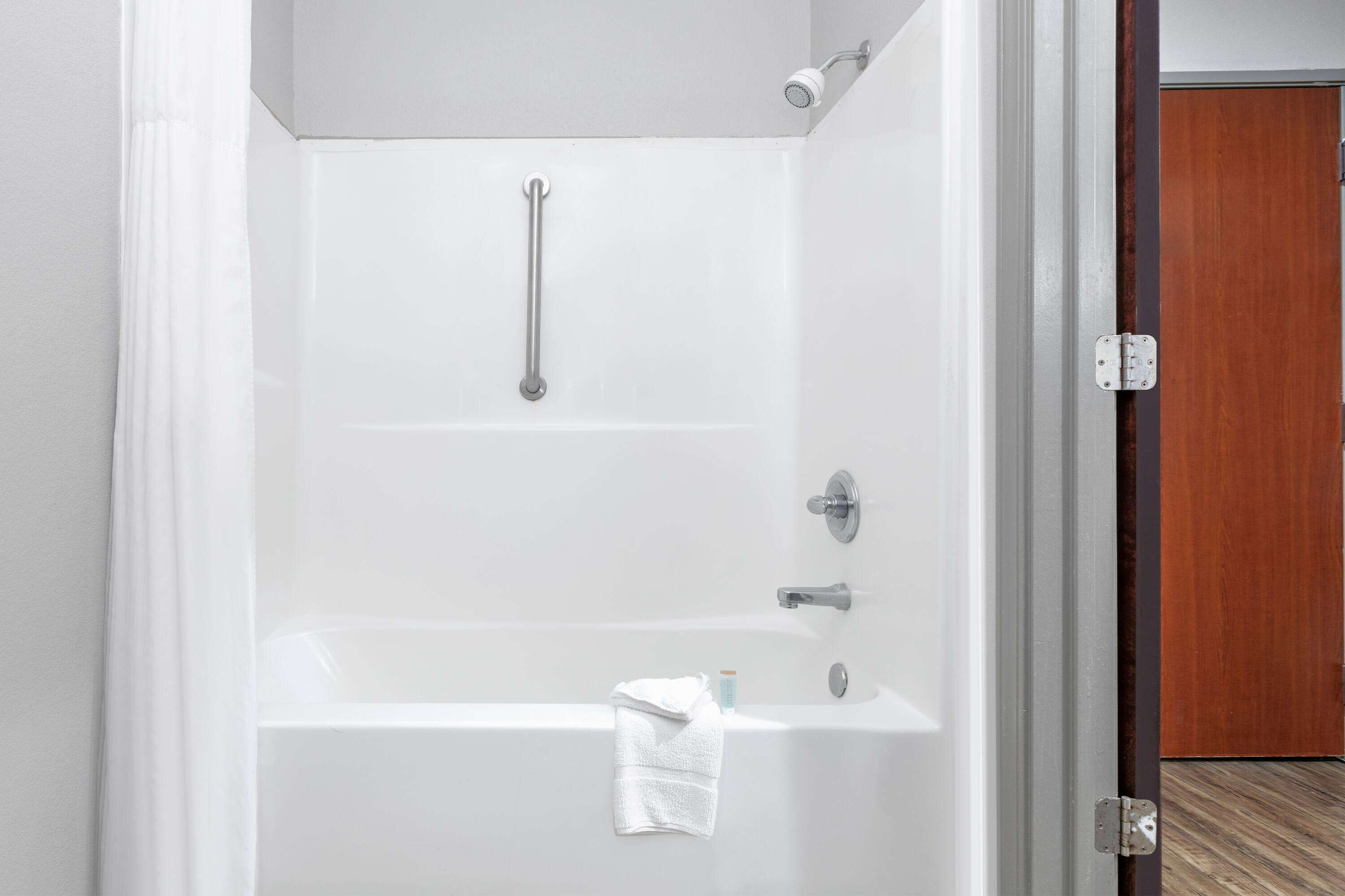 A modern bathroom with a white bathtub, a handheld showerhead, and a towel rack.