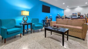 A room with a blue wall, a patterned sofa, two teal armchairs, a coffee station, and a small table with a lamp. - Days Inn & Suites by Wyndham Cabot (Cabot)