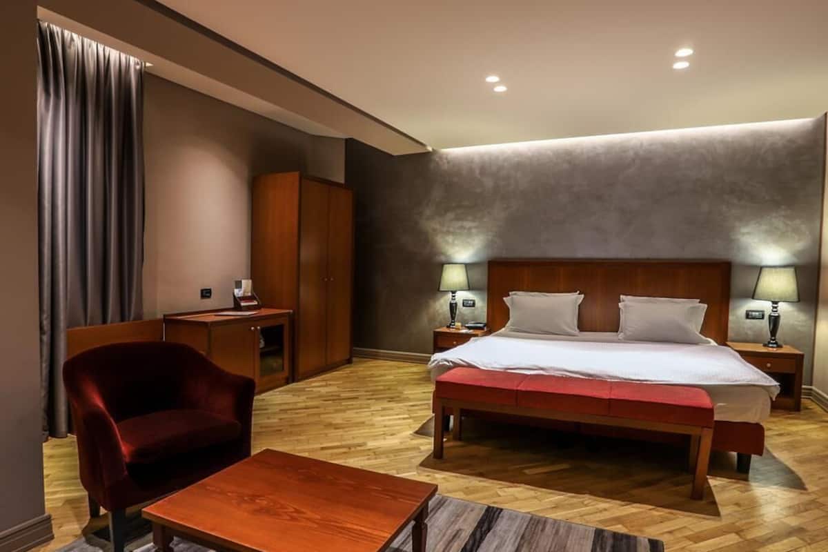 Una habitación de hotel con cama, escritorio, silla y mesita de noche con lámparas.