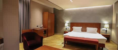 Habitación de hotel con una cama grande, dos mesitas de noche con lámparas, un escritorio de madera, una silla roja y una pequeña mesa.