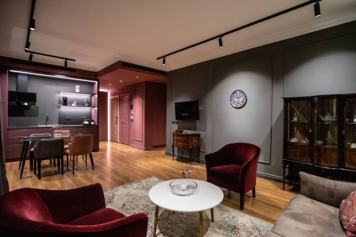 A modern living room with a dining area, a red armchair, a white coffee table, and a television on the wall.