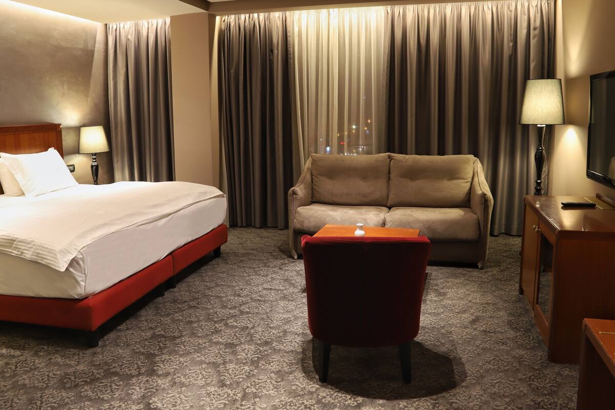 A hotel room with a bed, a sofa, a small table, and a TV.