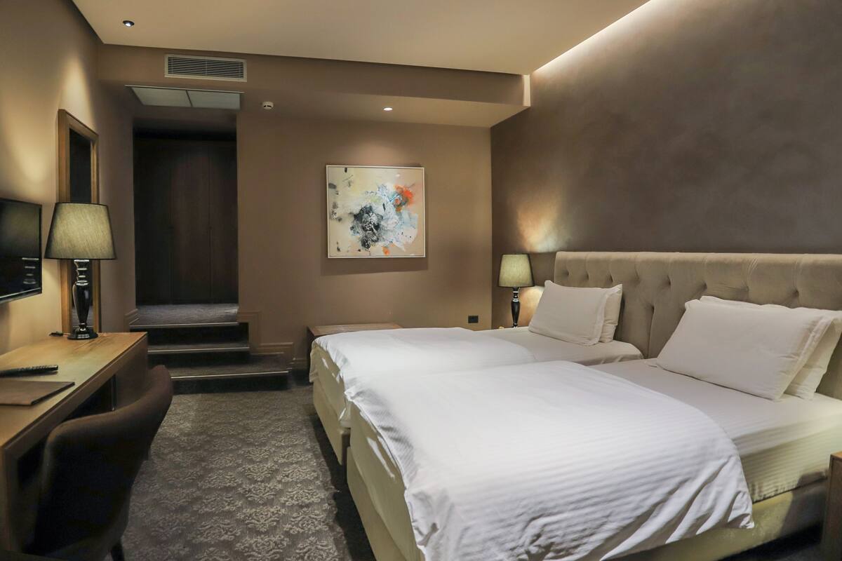 A hotel room with a large bed, a desk, a chair, a TV, and a painting on the wall.