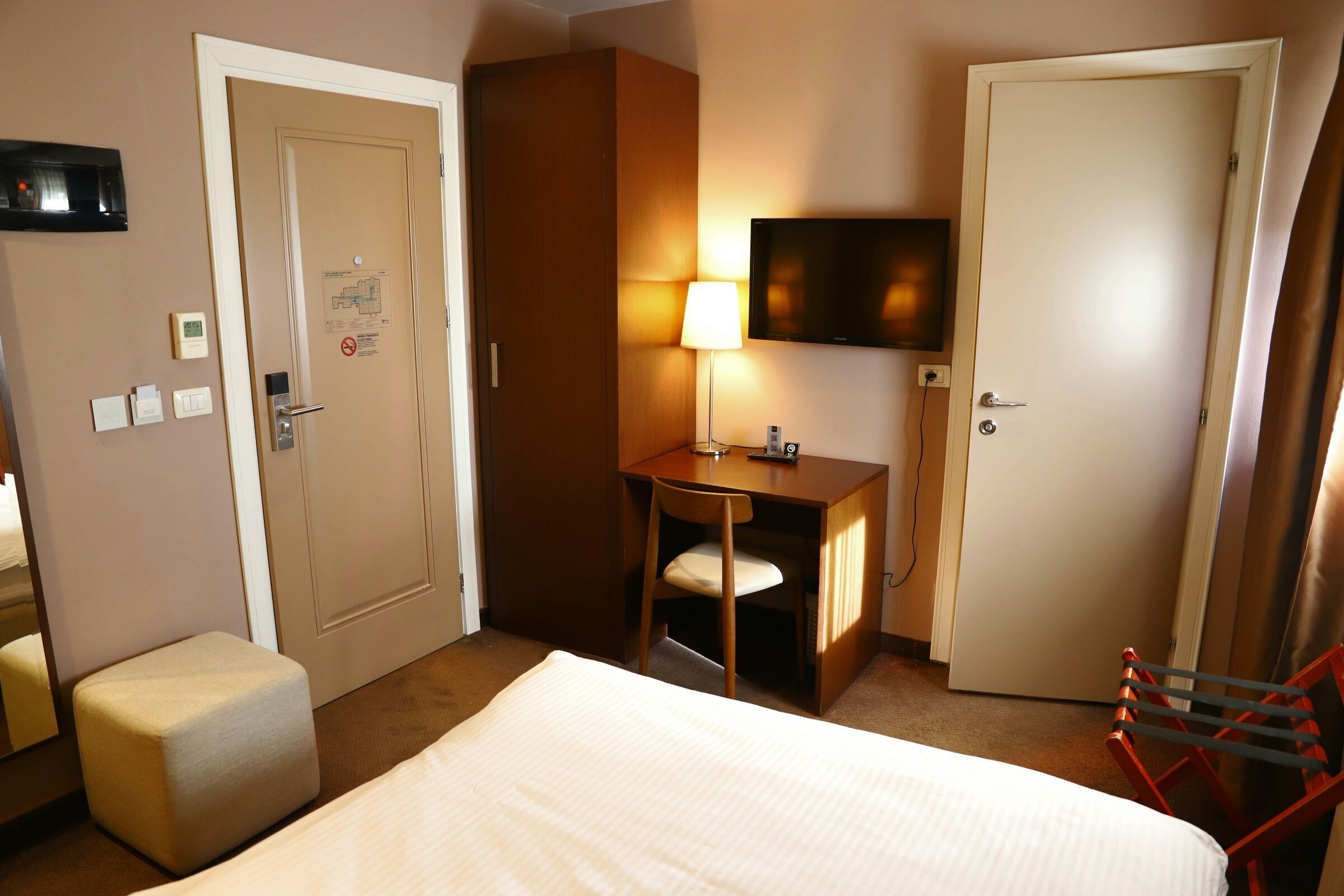Een hotelkamer met een bed, een bureau met stoel, een aan de muur bevestigde televisie en een deur.