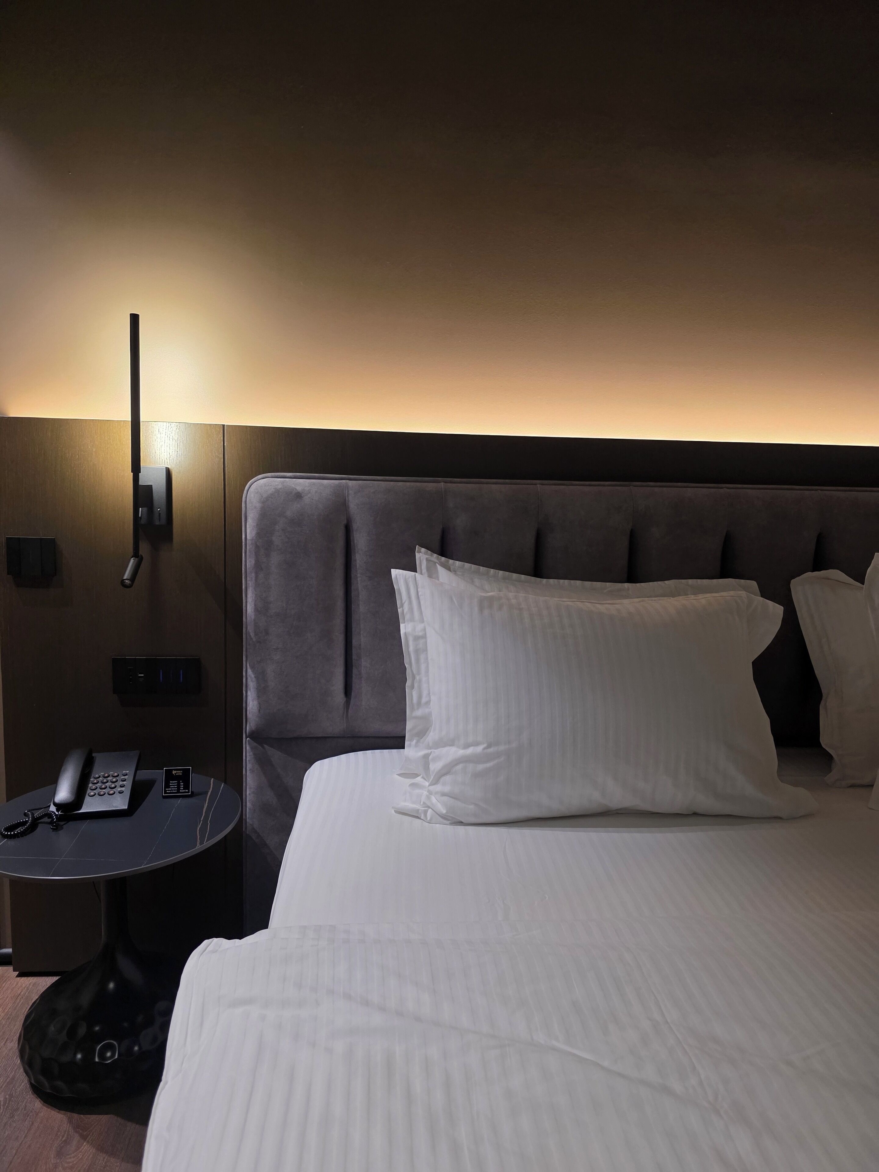 Ein Hotelzimmer mit einem großen Bett, einem Nachttisch mit Telefon und einer Wandleuchte.