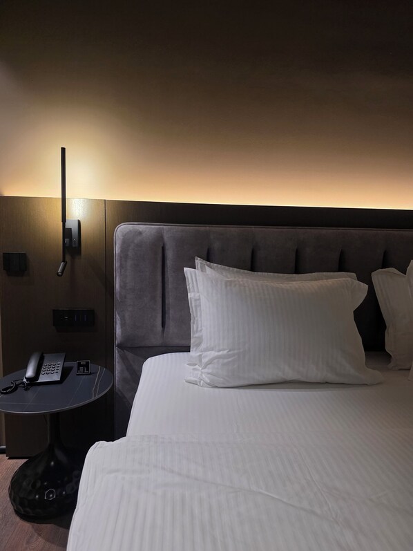 Une chambre d’hôtel avec un grand lit, une table de chevet avec un téléphone et une lampe fixée au mur.