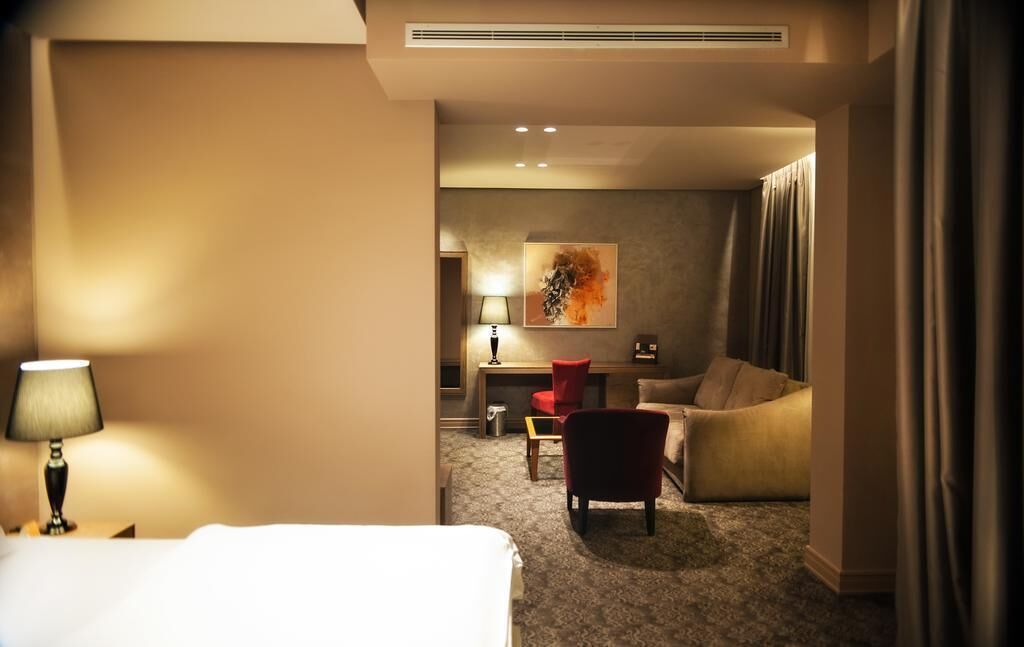 Ein Hotelzimmer mit Bett, Schreibtisch, Sessel, Sofa und Lampe.