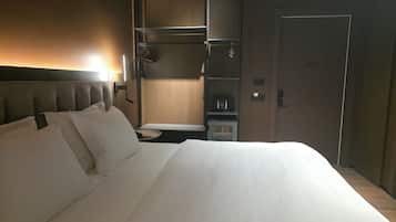 A hotel room with a large bed, a bedside table, a wardrobe, and a minibar.