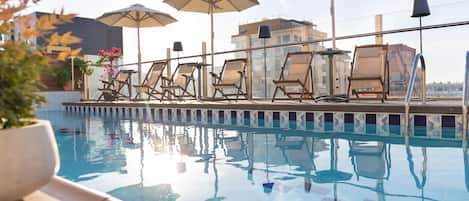 A rooftop pool with lounge chairs and umbrellas, surrounded by buildings.