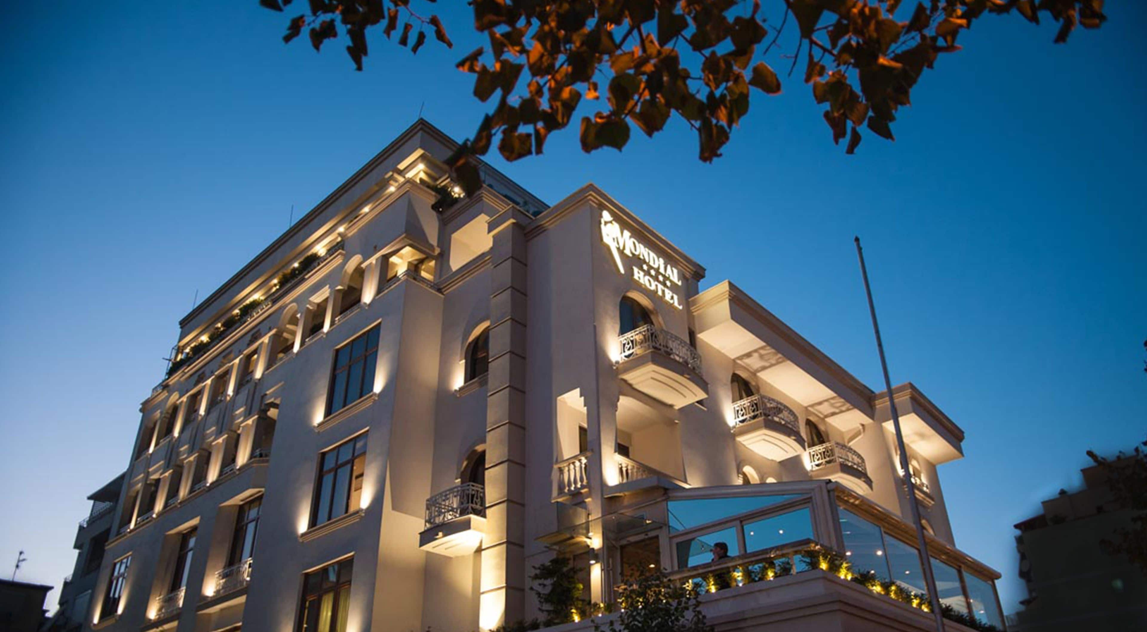A multi-story hotel with a prominent sign reading "Mondial Hotel." The building features multiple balconies and large windows.