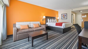 A hotel room with a bed, a sofa, a coffee table, and a desk. - Crossroads Hotel at Huron Event Center (Huron)