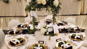 A round table set with white tablecloths, gold and black tableware, and a centerpiece of white flowers. - Crossroads Hotel at Huron Event Center (Huron)