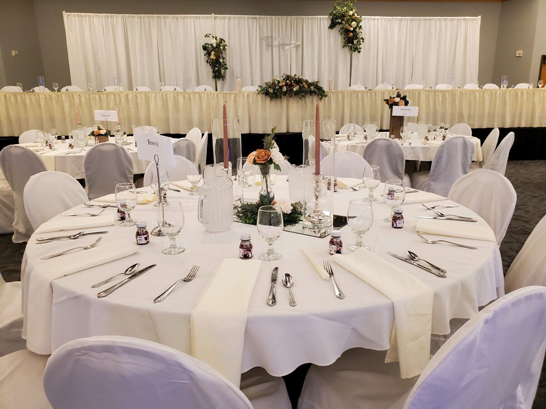 Un salón de banquetes con mesas redondas dispuestas para un evento formal, con manteles blancos, cristalería y centros de mesa florales.