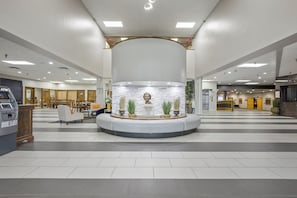 A spacious lobby with a central seating area, a reception desk, and an ATM machine. - Crossroads Hotel at Huron Event Center (Huron)