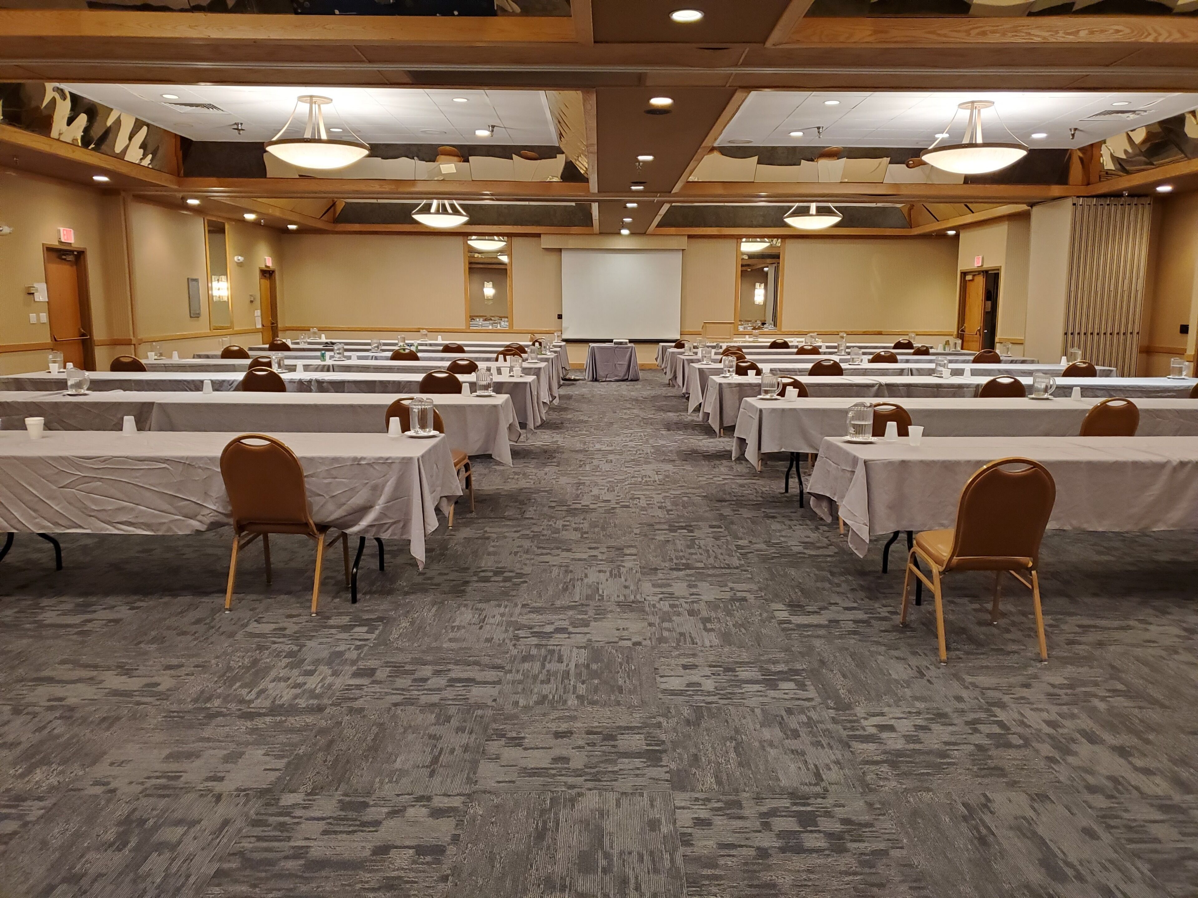 A conference room with rows of tables and chairs, a projector screen, and a carpeted floor.