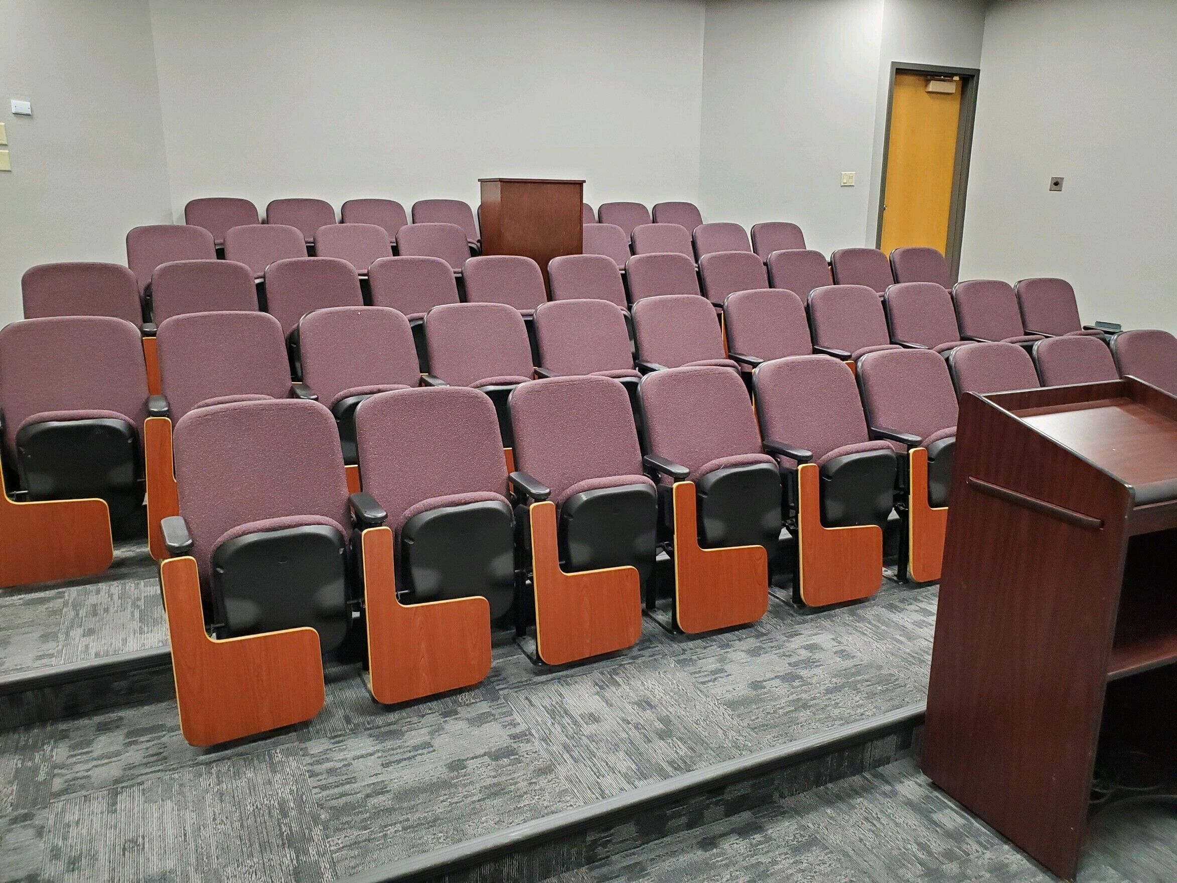 A conference room with rows of chairs, a podium, and a door.